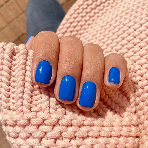 Short gel nails in cobalt blue on a pink knit