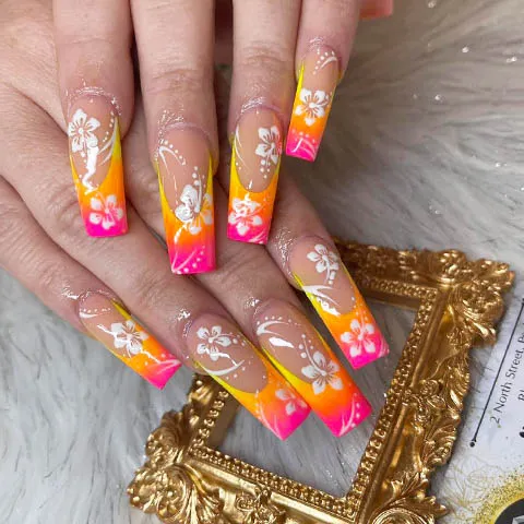 Long nails with an orange and pink ombre and white flowers
